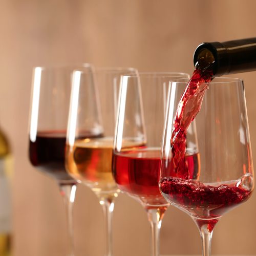 Pouring wine from bottle into glass on blurred background, closeup